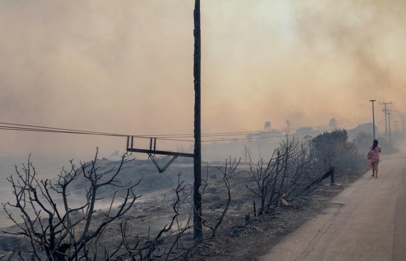 Una mujer camina entre el humo cerca de Lindos, arrasada tras el paso del incendio.