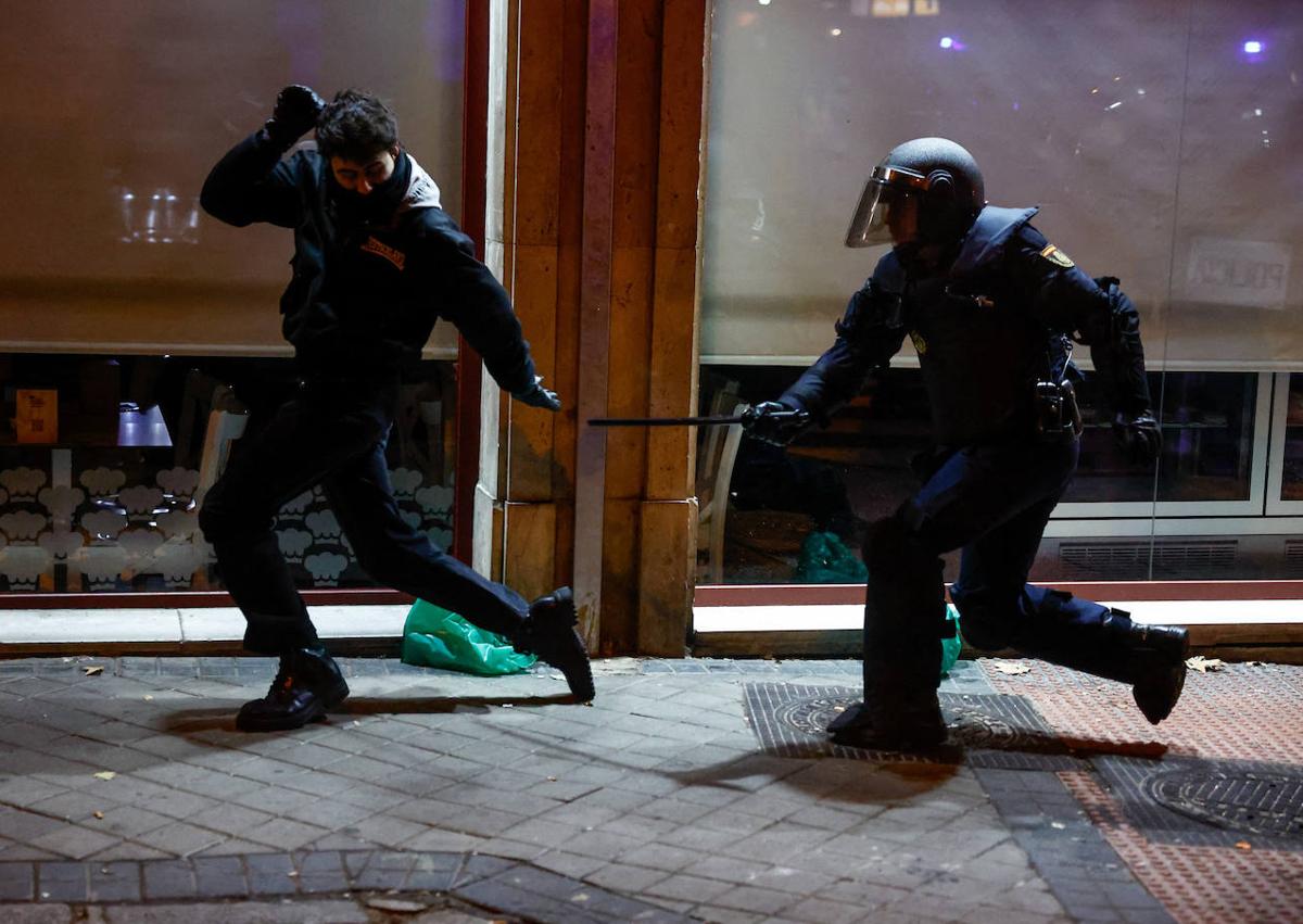 Imagen secundaria 1 - En la imagen superior, los agentes tratan de alejar a los manifestantes tras un primer conato de carga; en la foto siguiente, un antidisturbios persigue a un joven que estaba en la zona de los alborotadores y, por último, varios policías detienen a uno de los sospechosos de los altercados violentos mientras detras suyo arde un contenedor incendiado por los ultras en la calle Ferraz.