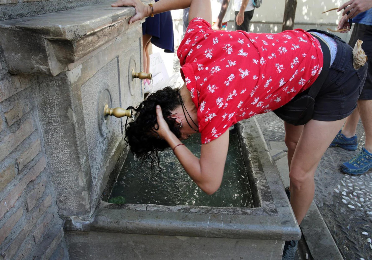 Una joven se refresca en la fuente de un aljibe en el barrio granadino del Albaicín.