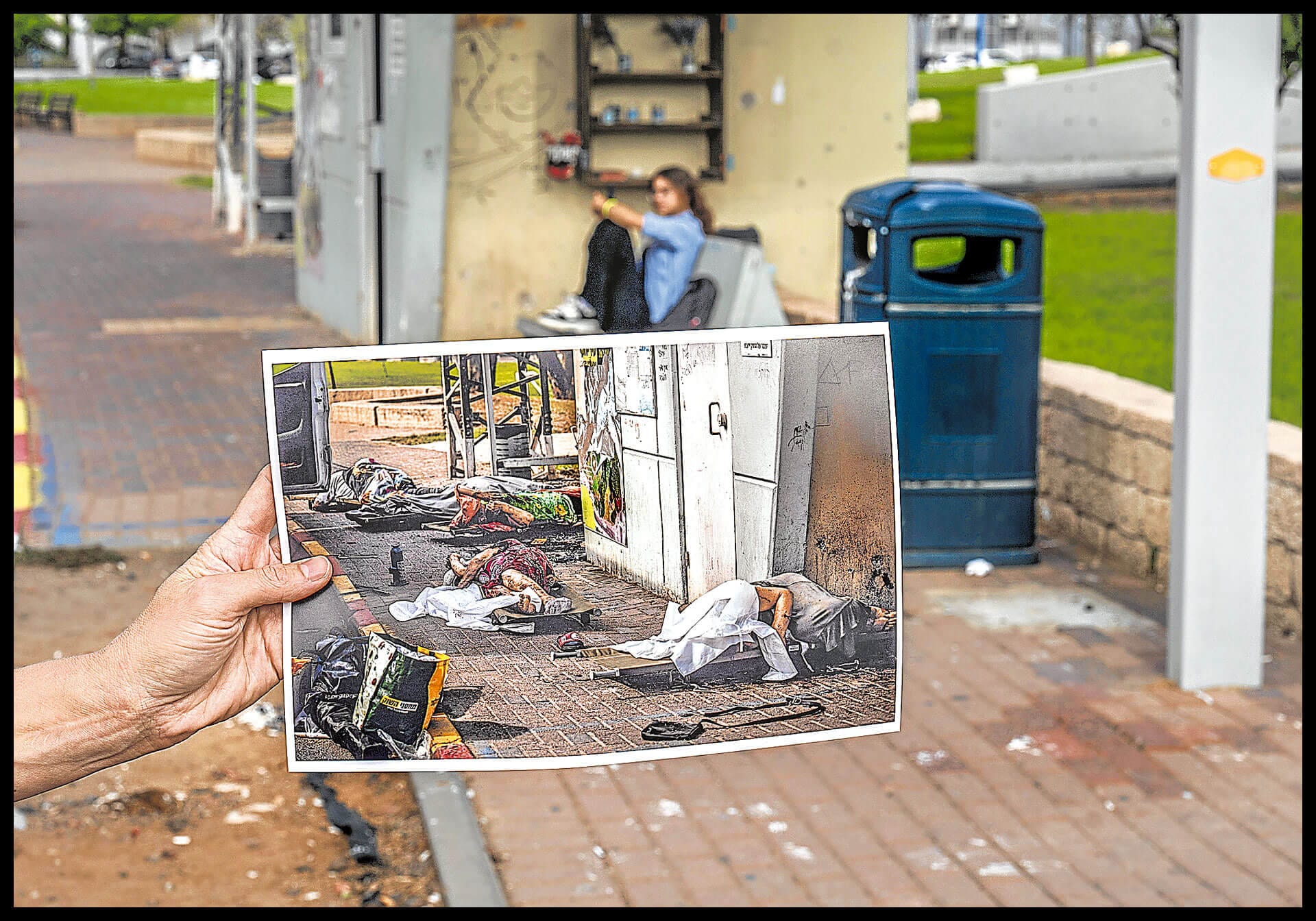 Una mujer muestra la fotografía de cadáveres de israelíes en la parada de autobús de Sderot tras los ataques del 7 de octubre de 2023,, en una imagen tomada en el mismo lugar el pasado 26 de septiembre.