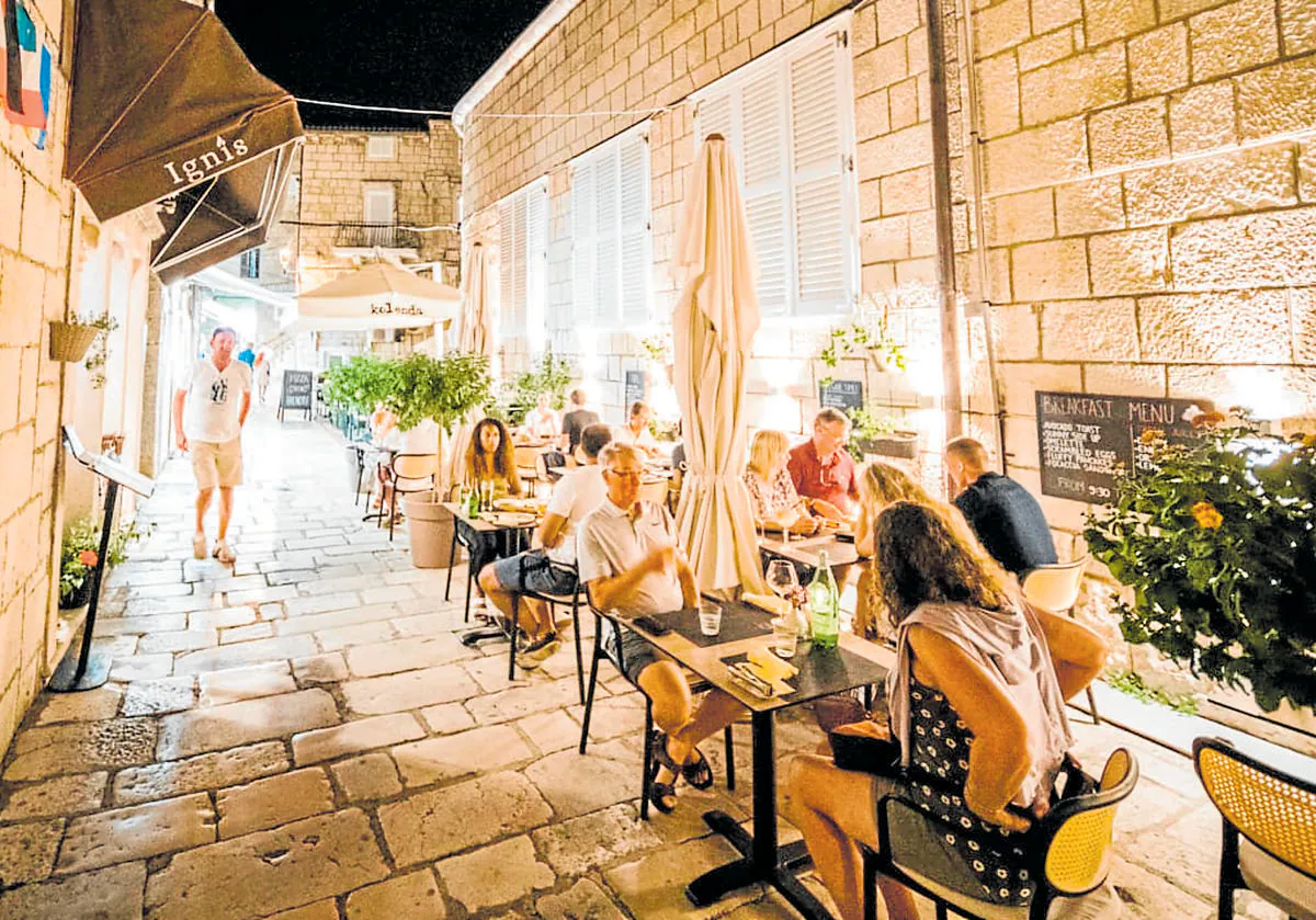 Imagen principal - Arriba: Terraza de Ignis, en una de las características calles empedradas de la isla de Korcula. Abajo: Último toque a las berenjenas en tempura con miel OPG Komparak (de la isla) y queso de cabra local, Pilar ajusta el delantal a su pareja, Vicko.