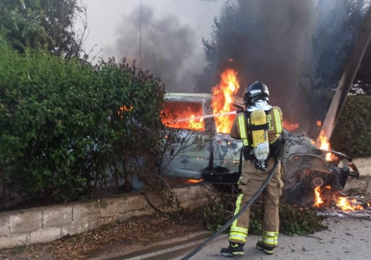 Um bombero apaga las llamas del coche.