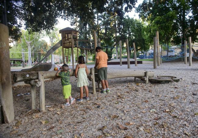Tierra, árboles, agua. Unos niños juegan en el jardín de la Pólvora de Murcia con una canalización de agua, en un espacio marcado por el suelo de zahorra y las sombras que proyecta el arbolado.