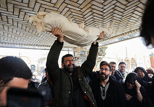 Un padre levanta el cadáver de su hija, de dos años, muerta en un ataque de EE UU contra Teherán.