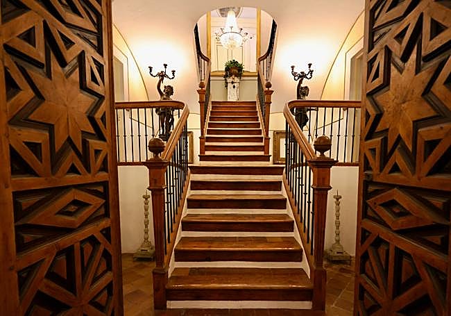 Escalera principal de acceso al edificio, con maderas nobles y decoración de época.